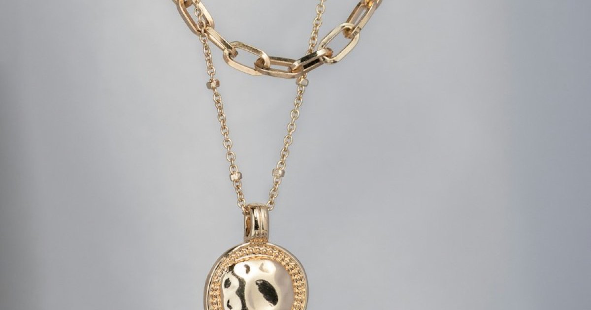 Gold layered necklace set with a round hammered pendant, styled as a JewelVisuals catalog photograph on a soft gray background